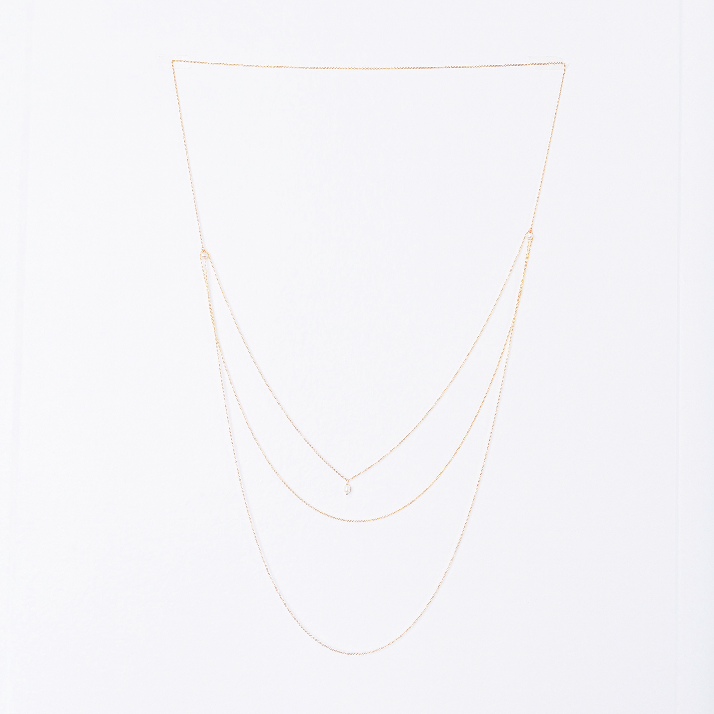 Front and back view of a long necklace with three loops, featuring white pearl beads